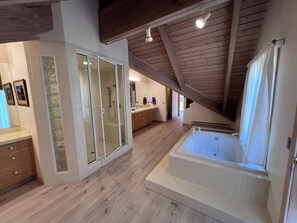A spacious bathroom with a walk-in shower, a bathtub, and wooden flooring.
