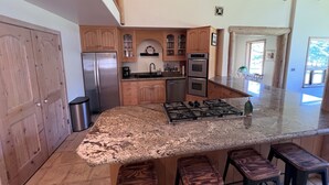 A kitchen with wooden cabinets, a stainless steel refrigerator, a double oven, and a granite countertop. - Luxurious Log Home Retreat (Hailey)