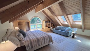 A spacious attic bedroom with a large bed, a sofa, a reading nook, and a skylight. - Luxurious Log Home Retreat (Hailey)