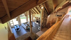 A spacious living area with a stone fireplace, wooden beams, and a view of the outdoors. - Luxurious Log Home Retreat (Hailey)