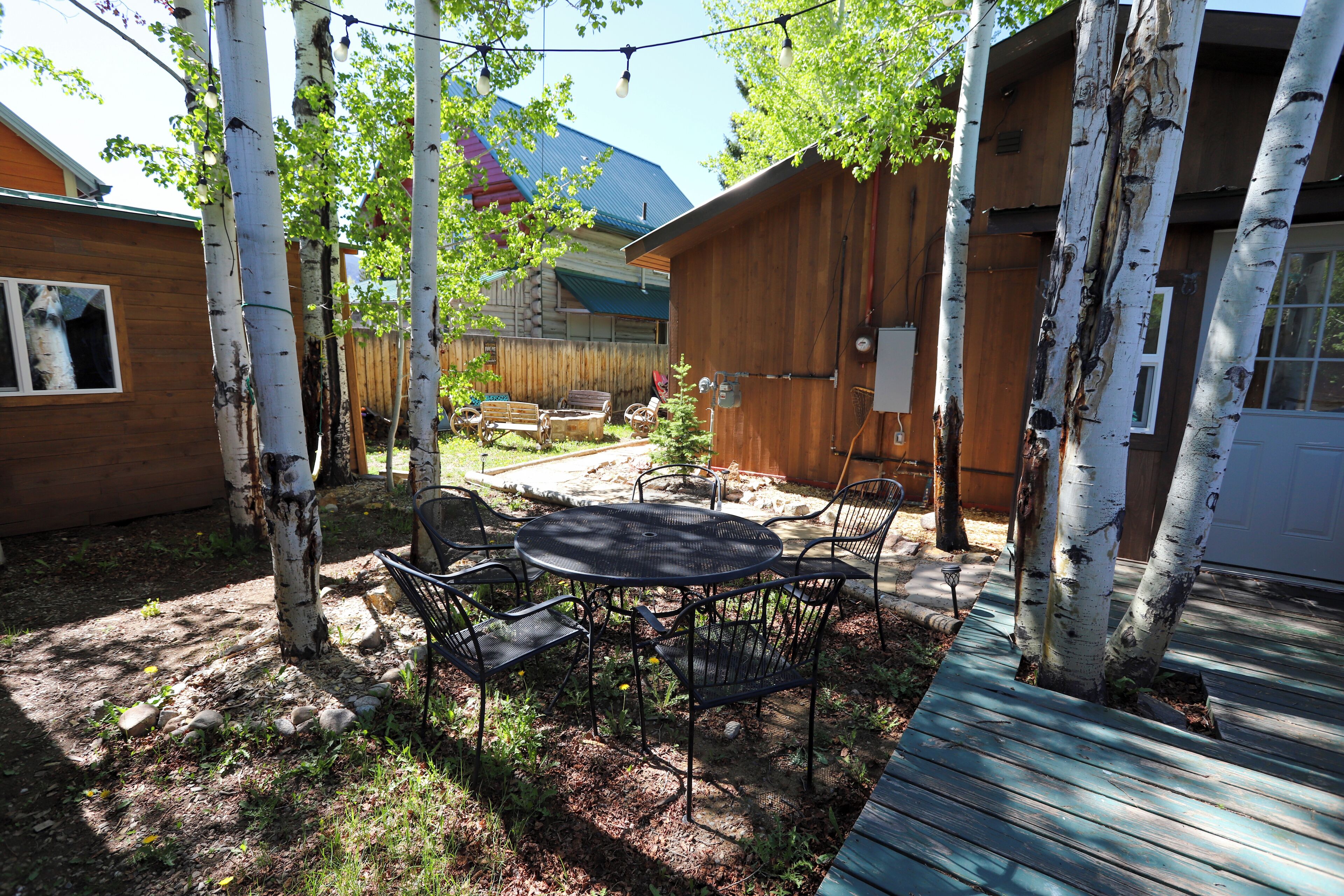 A backyard with a wooden deck, a round table with chairs, and birch trees.