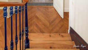 Un couloir doté d’un plancher en bois, d’un lustre et d’une vue sur une pièce avec une porte.