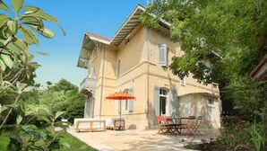 Une maison à deux étages dotée d’un balcon, d’une terrasse avec des meubles d’extérieur et d’un jardin.