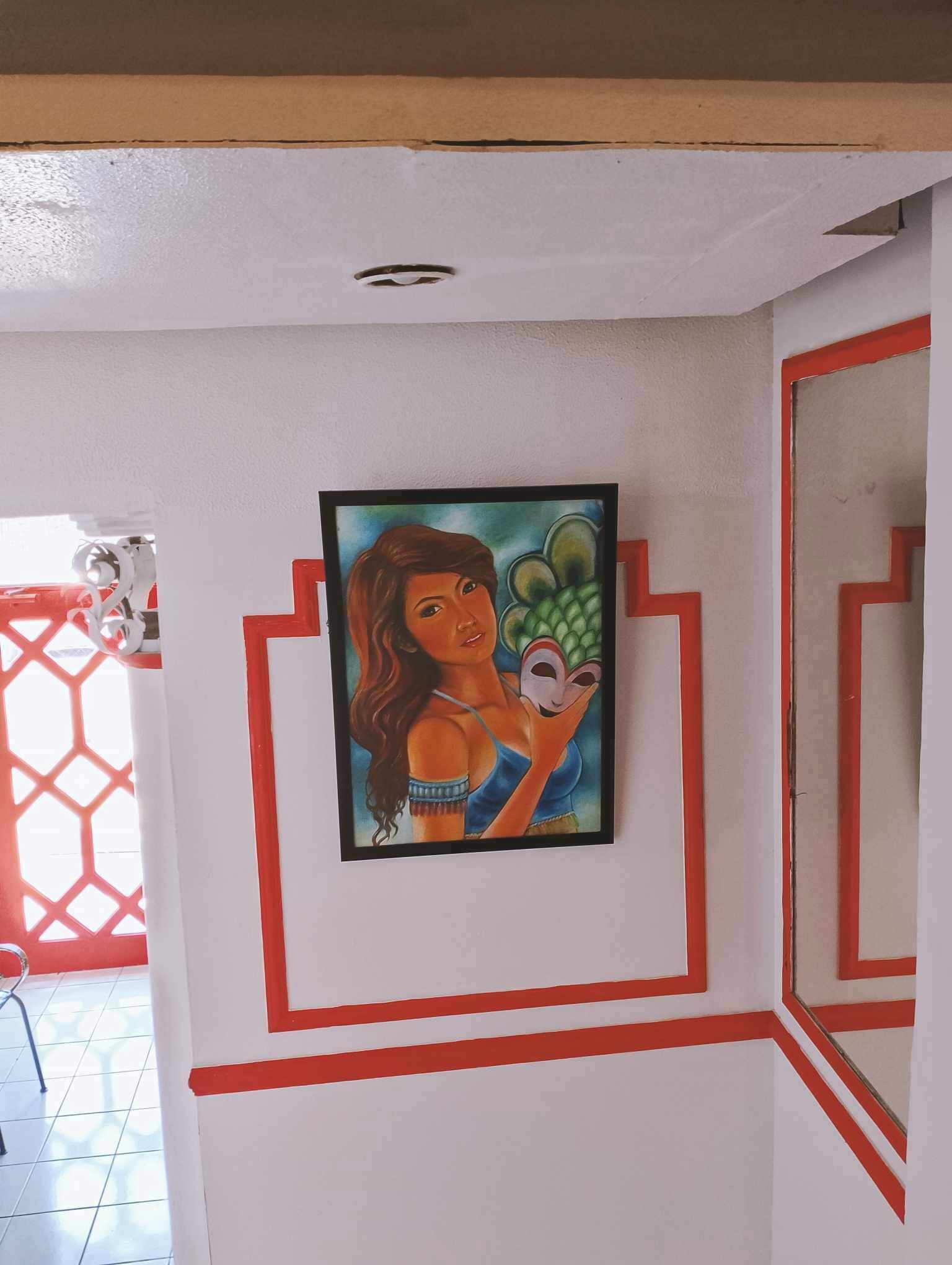 A room with a white wall featuring a framed painting of a woman holding a mask.
