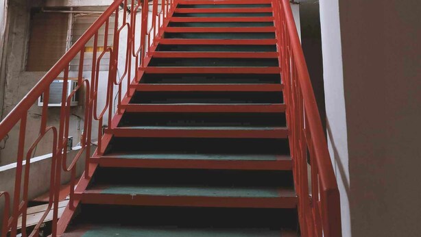 Eine Treppe mit roten Geländern führt zu einer Zwischenebene mit weißer Decke und Oberlicht.