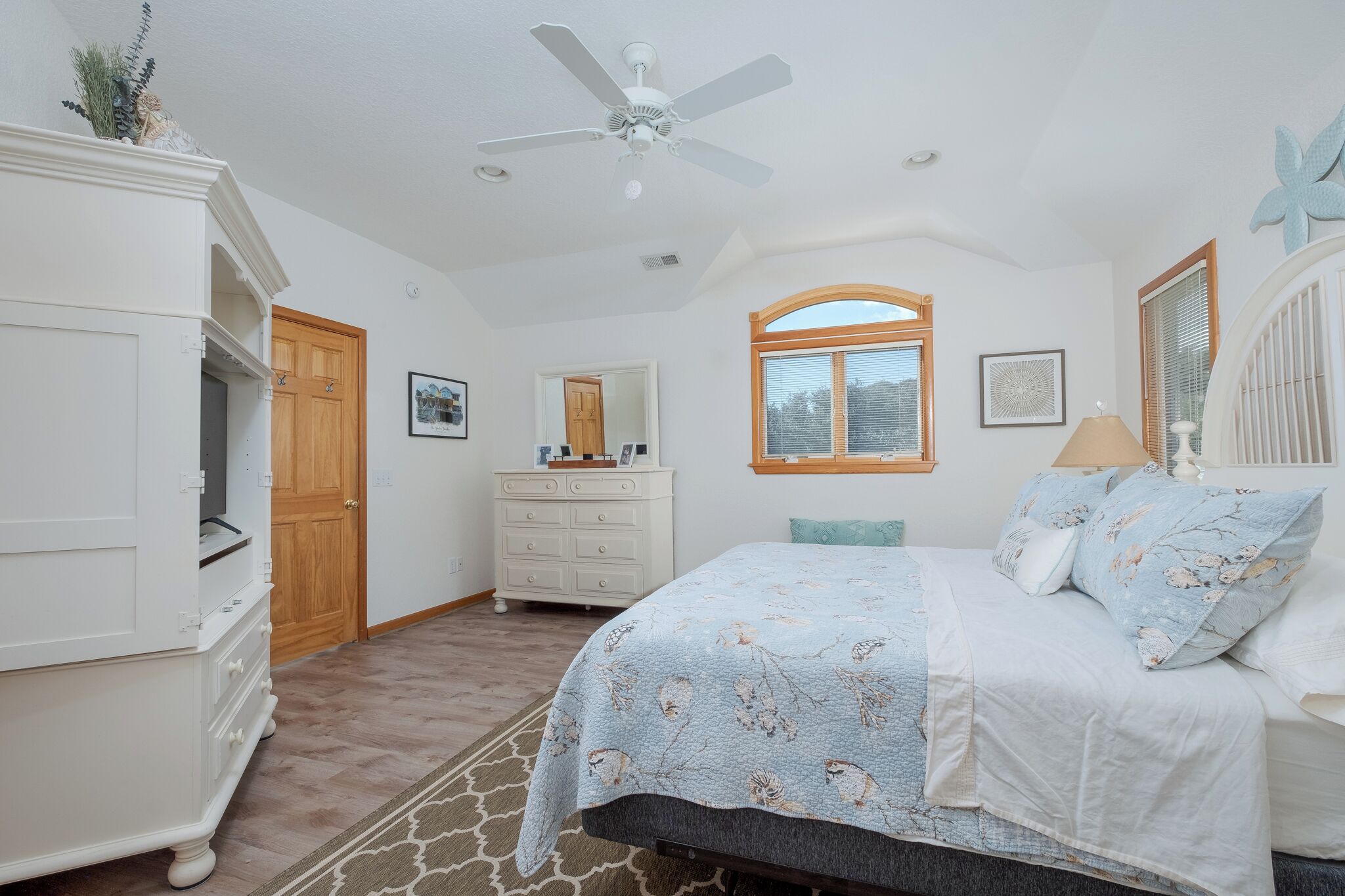 A bedroom with a bed, dresser, vanity, and a ceiling fan.