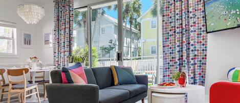 A modern living room with a gray sofa, wooden chairs, a white coffee table, and colorful curtains.