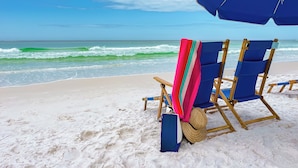 Une scène de plage avec deux chaises de plage bleues, une serviette colorée et un parasol bleu.