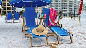Une plage avec des chaises longues bleues et un chapeau de paille posé sur l’une d’elles.
