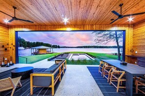 Un interior moderno con un ventanal grande con vista a un lago, techo de madera y una zona de estar con mesas y sillas.