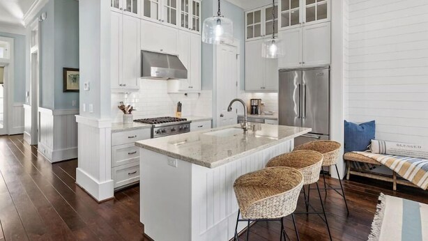 Una cocina amplia con armarios blancos, una isla grande con taburetes de bar y un refrigerador de acero inoxidable.