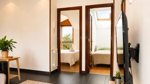 A hotel room with a bed, a TV, a small table with a plant, and a view of the outside balcony.