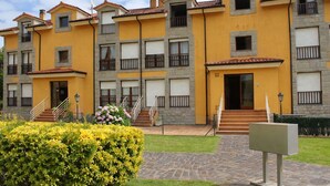 A multi-story building with balconies, a central entrance, and a paved courtyard.