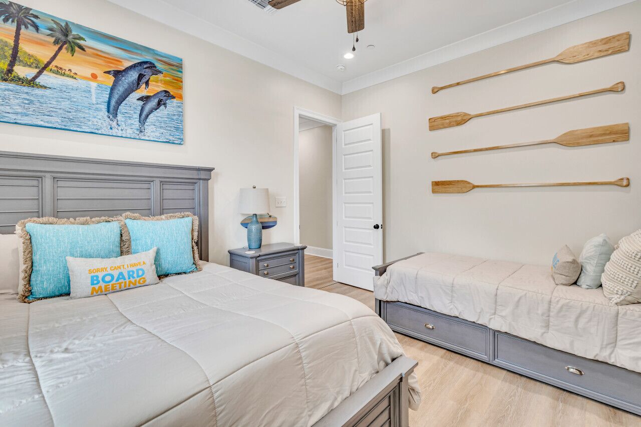 Un dormitorio con una cama grande, una cama más pequeña, una mesita de noche, una lámpara, un cuadro de delfines y remo en la pared.