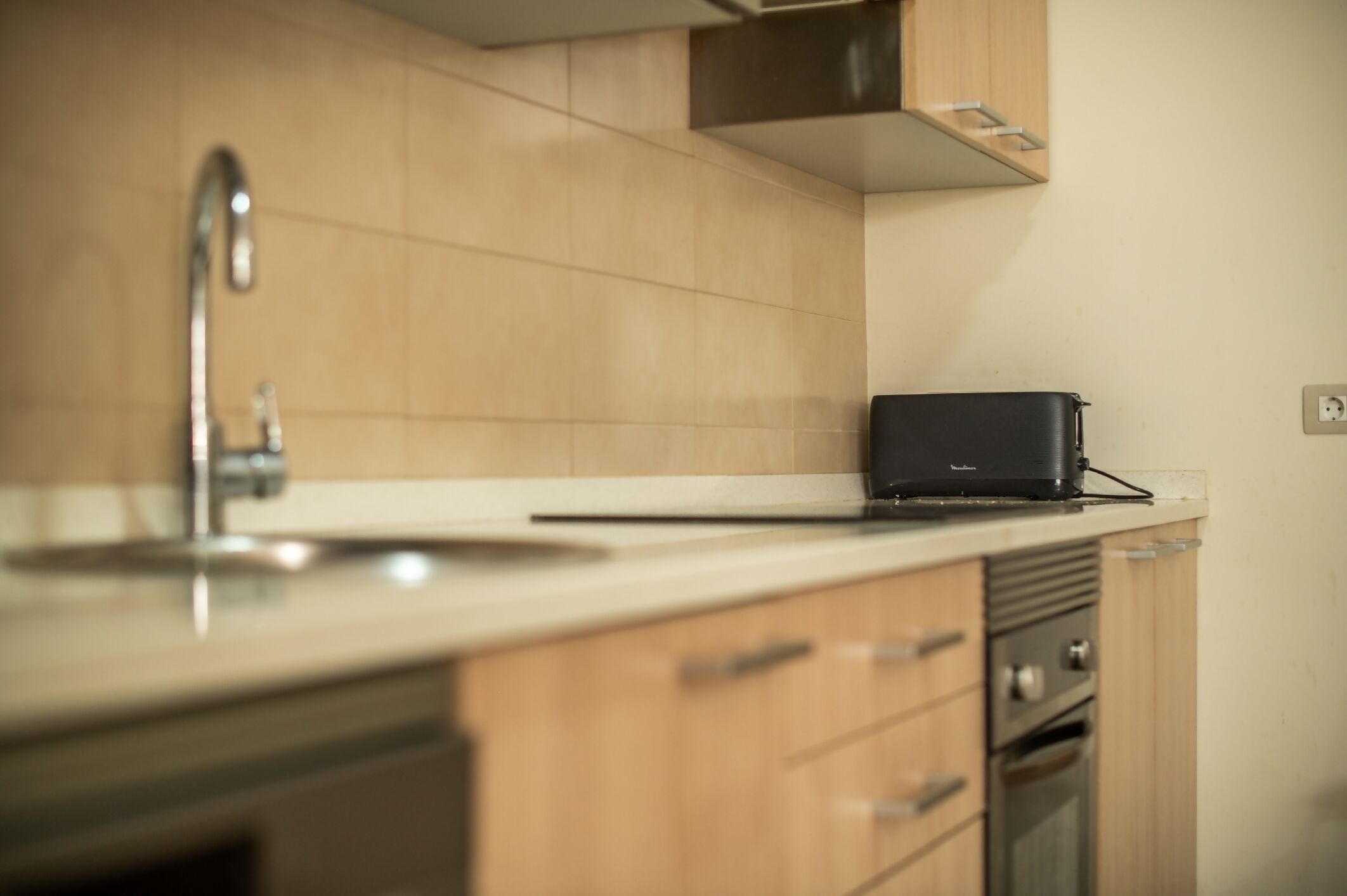 A kitchen with a sink, a black portable appliance, wooden cabinets, and a stainless steel oven.