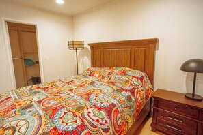 Um quarto com uma cama, mesa de cabeceira, cômoda e armário.