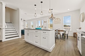 A modern kitchen with white cabinetry, a central island, pendant lighting, a dining area with a table and chairs, and a staircase leading to another level. - ☀️Private Pool~Sleeps 16~Front & Back Porch~Walk 2 Beach~Pet Friendly~Sealah🏖️ (Destin)