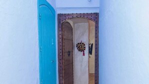 Un pasillo estrecho con una puerta azul, suelo de baldosas con diseños y un arco decorativo que da a una habitación.