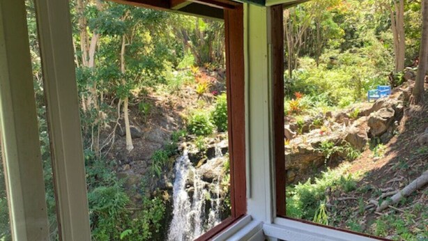 Une fenêtre donnant sur une cascade, elle-même entourée d’une végétation luxuriante.