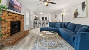A living room with a brick fireplace, a blue sofa, a round coffee table, and a ceiling fan. - The Pine Grove Retreat (Ladson)