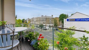 A balcony with a table and chairs, overlooking a street with buildings and a Safestore sign. - London Oasis Retreat With 2 Bedrooms - Fulham (London)