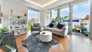 A modern living room with a sofa, a patterned armchair, a coffee table, and a glass door leading outside. - London Oasis Retreat With 2 Bedrooms - Fulham (London)