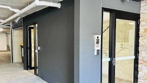 A modern building with a concrete floor, a black door, and a security camera. - Spacious Family 3BR Top-Floor Stay | Views, 2-Car Parking & EV-Friendly (Mount Gravatt East)