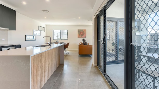 A modern kitchen with a central island, a dining area with a sofa, and a view through a glass door. - Spacious Family 3BR Top-Floor Stay | Views, 2-Car Parking & EV-Friendly (Mount Gravatt East)