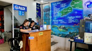 Een receptiegedeelte met een houten balie, twee medewerkers, een kaart van Panglao Island en een waterdispenser.