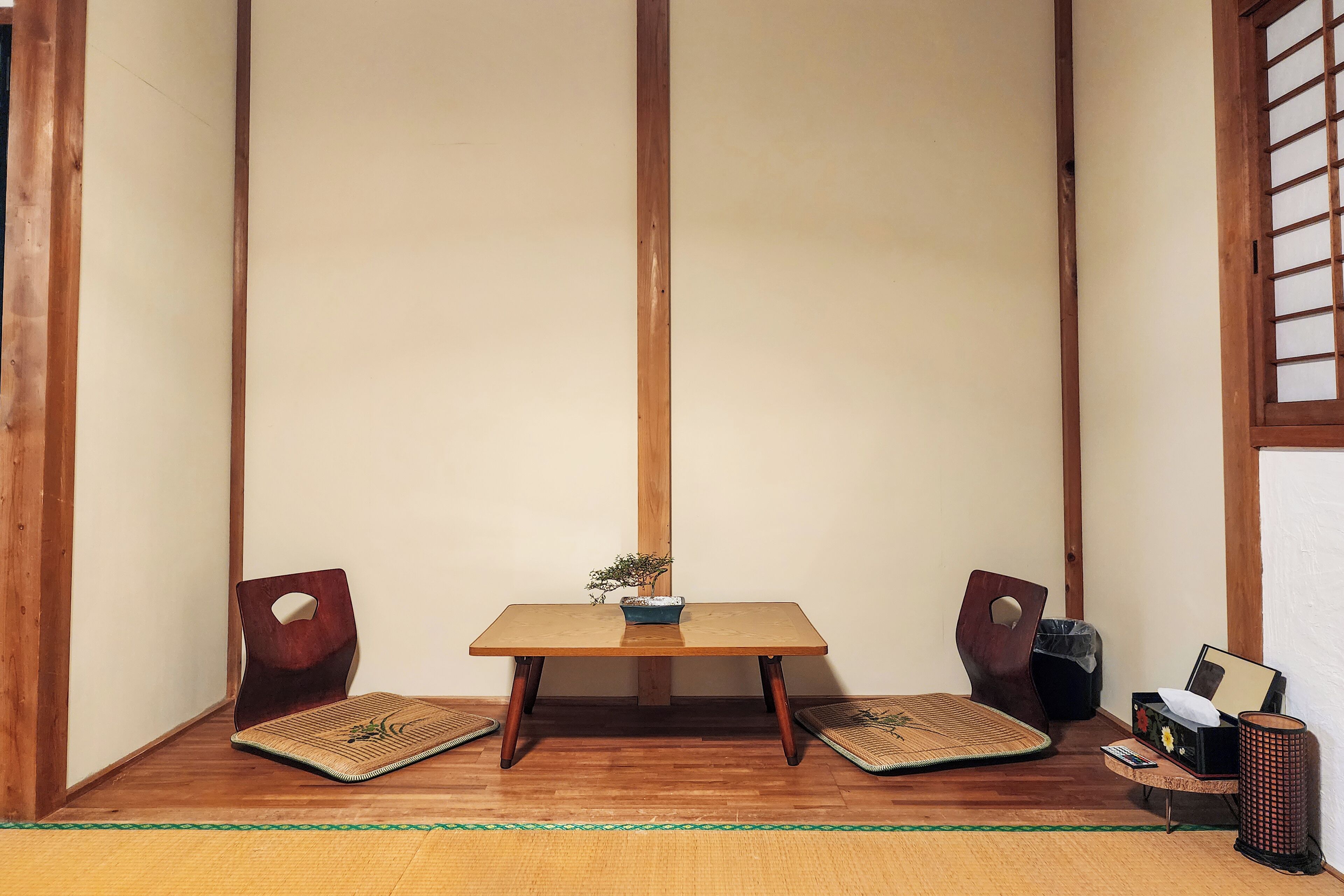 Una habitación japonesa tradicional con suelo de tatami, una mesa de madera baja y dos sillas de madera.
