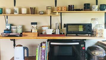 A kitchen with a microwave, kettle, and coffee maker on the counter. Shelves above hold various mugs and decorative items.