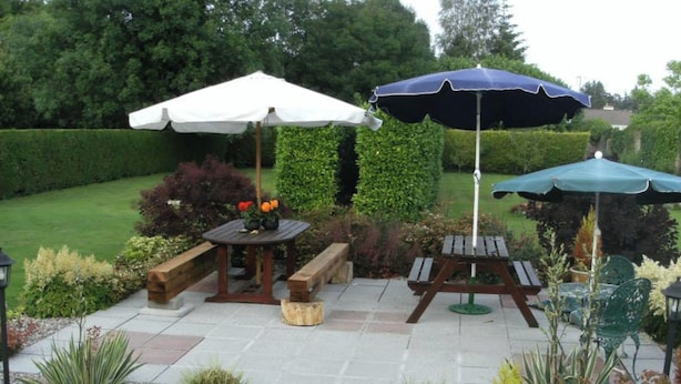 An outdoor patio with two wooden tables, benches, and umbrellas. - The Railway Lodge, 4 Bedrooms, Sleeps 11, Pets Ok (Moate)