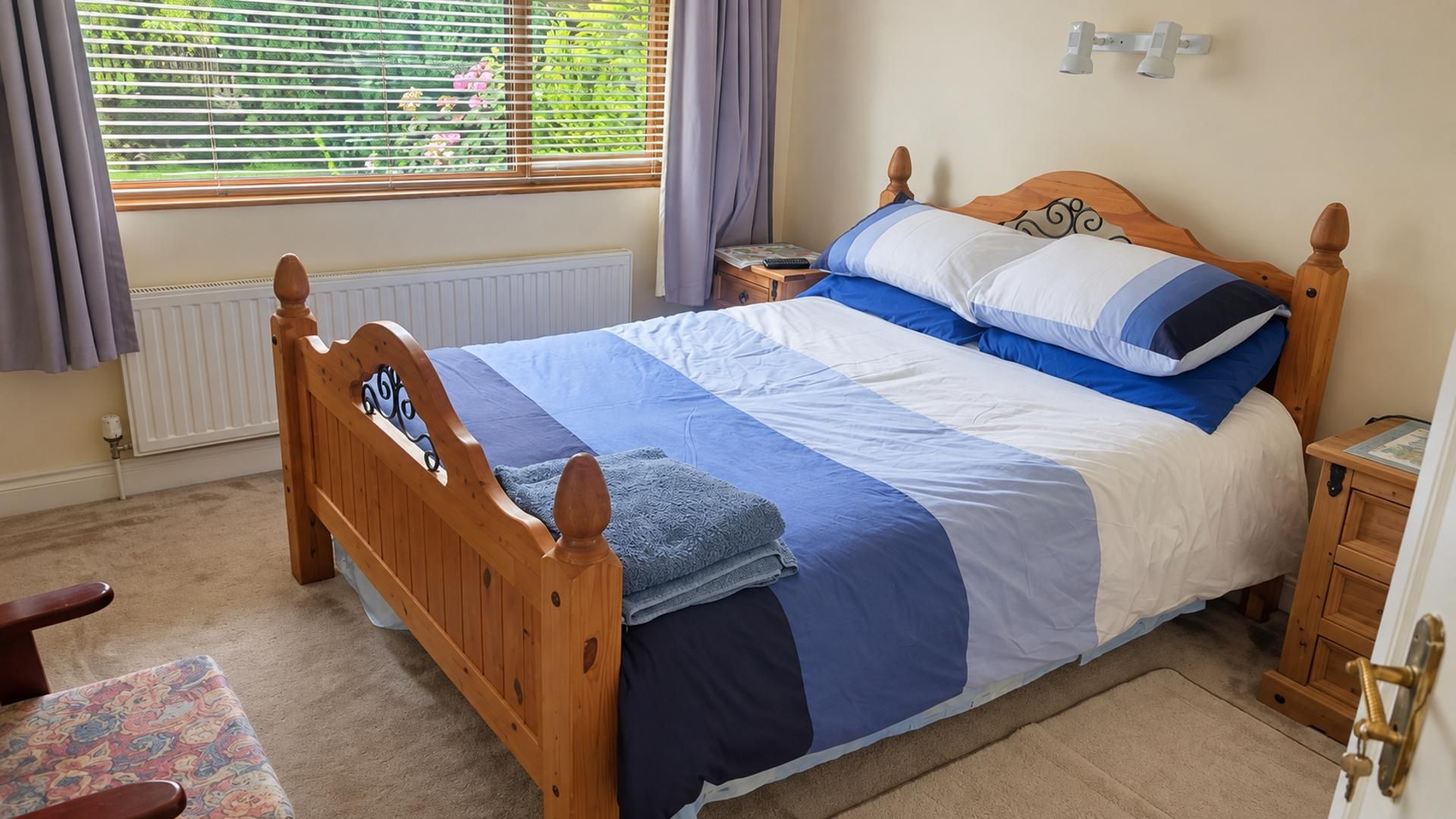 A bedroom with a wooden bed, a nightstand, a chair, a radiator, and a window with curtains.