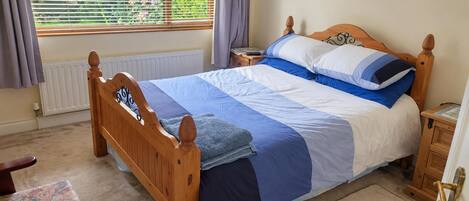Une chambre à coucher avec un lit en bois, une table de chevet, une chaise, un radiateur et une fenêtre avec des rideaux.