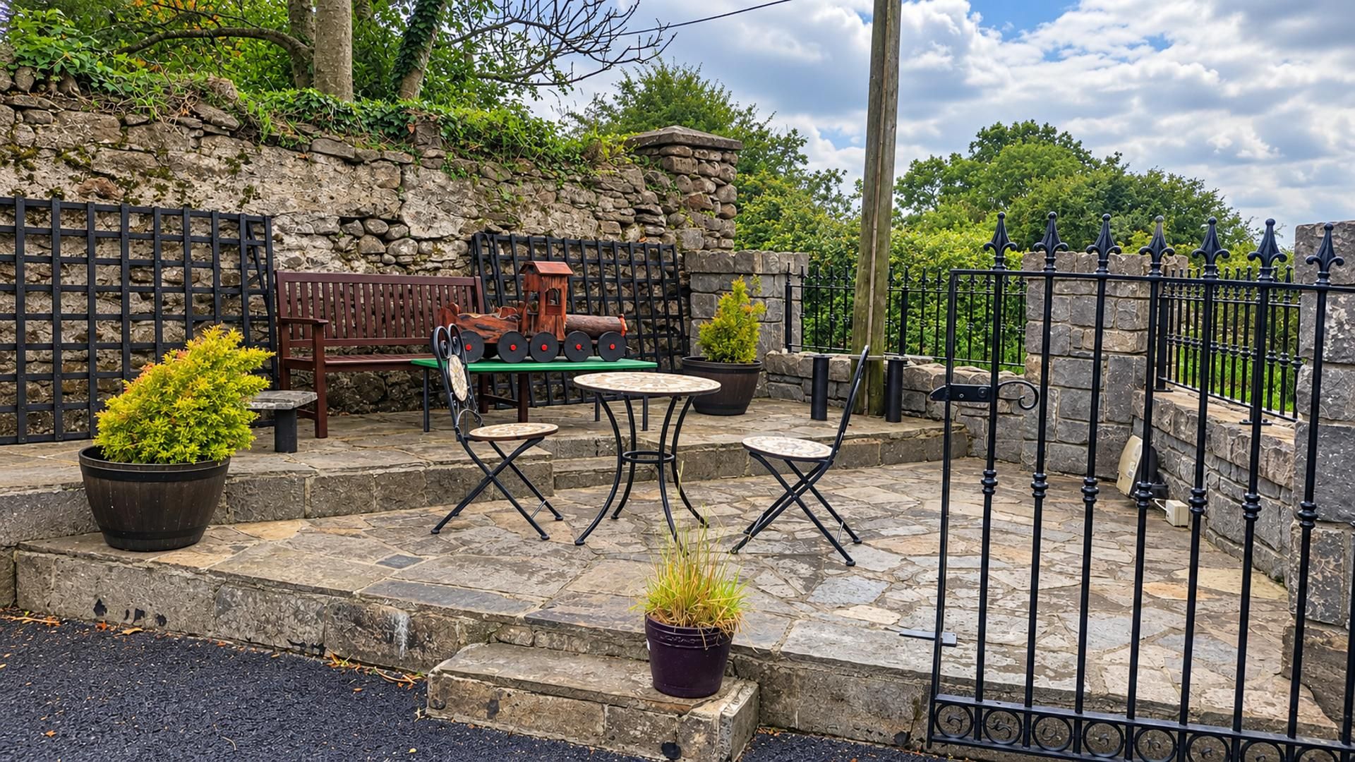 An outdoor patio with stone flooring, metal fencing, and potted plants.