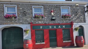 A building with a sign reading "P. EGAN" and a green door. There are flower baskets on the windowsills and two barrels on the ground. - The Railway Lodge, 4 Bedrooms, Sleeps 11, Pets Ok (Moate)