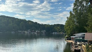 A calm lake with docked boats, a wooden pier, and a forested hillside in the background. - Sleep Lakeside in Our Cozy Boathouse with Mtn Views (Landrum)