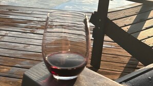 A glass of red wine on a wooden table by a body of water. - Sleep Lakeside in Our Cozy Boathouse with Mtn Views (Landrum)