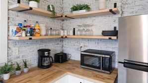 A kitchen with wooden shelves, a coffee maker, a microwave, and a refrigerator.
