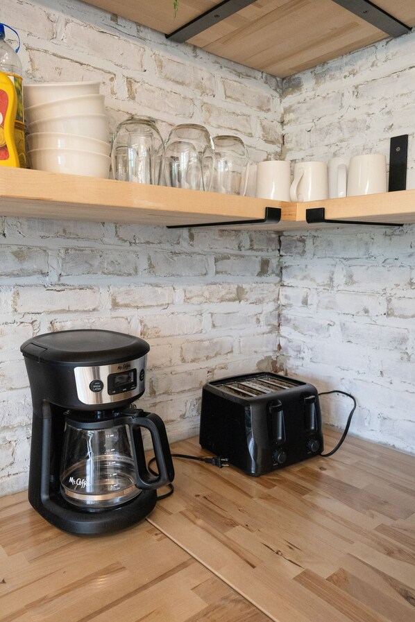 Una cocina equipada con cafetera, tostadora y una alacena con vajilla y copas.