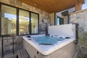 A hot tub with a stone exterior, a wooden ceiling, and a view of a house through large windows. - Panoramic Views, Downtown Access (Fraser)