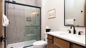Een moderne badkamer met een glazen douchecabine, een wit toilet, een houten wastafelmeubel met een wastafel en een grote spiegel.