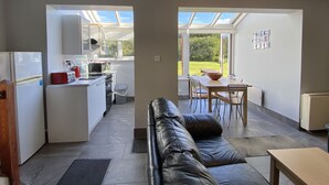 Une cuisine moderne avec un coin repas, un canapé en cuir et une vue sur le jardin grâce à de grandes fenêtres.