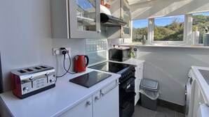 Une cuisine compacte équipée d’un four à micro-ondes, d’un grille-pain et d’une bouilloire sur un plan de travail blanc, ainsi que d’une cuisinière et d’une poubelle.