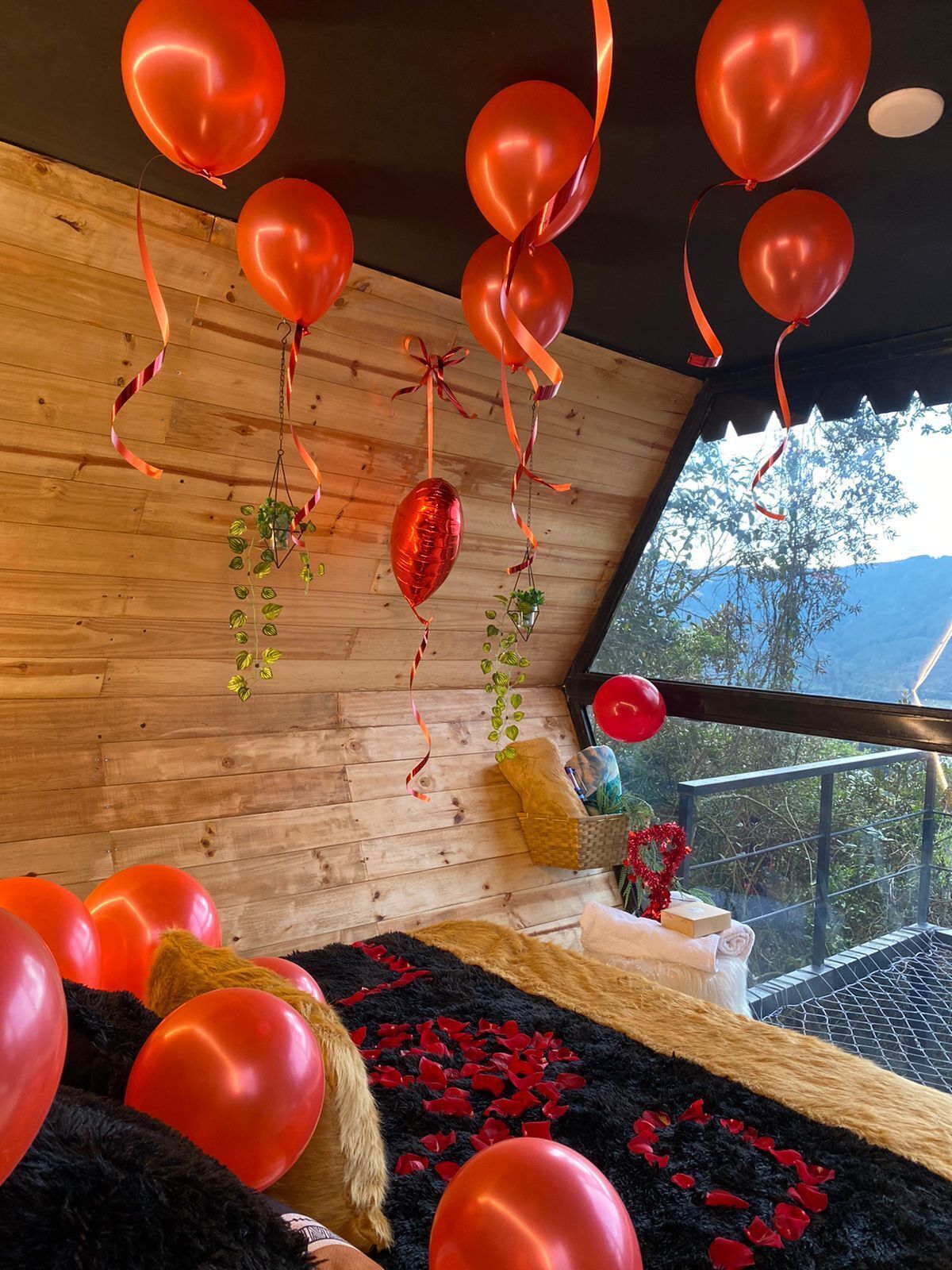 Una habitación con paredes de madera, un ventanal grande y varios globos rojos.