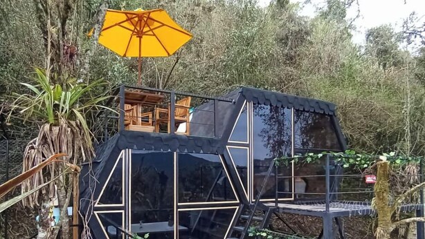 A treehouse with a wooden deck, a small enclosed area, and a yellow umbrella. - Laguna Glamping (La Calera)