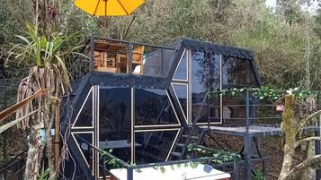 Una casa en un árbol con terraza de madera, un espacio cerrado pequeño y un paraguas amarillo.
