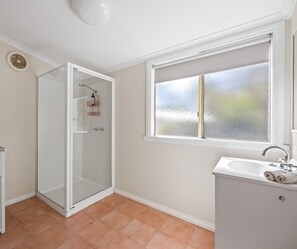 A bathroom with a glass shower enclosure, a window with frosted glass, and a white sink with a towel. - Orchid Lane Cottages (Dadswells Bridge)