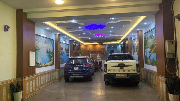 A hallway with two cars parked, a ceiling with recessed lighting, and wall-mounted paintings. - Hai Yen Hotel Pleiku by Bay Luxury (Hoi Phu)