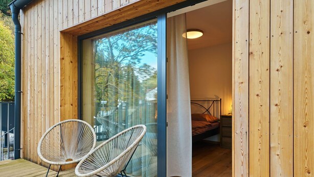 Une cabane en bois avec une porte en verre donnant sur une chambre à coucher équipée d’un lit et d’une table de chevet.